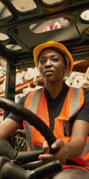 Confident young African female worker driving a forklift around the floor of a textile warehouse